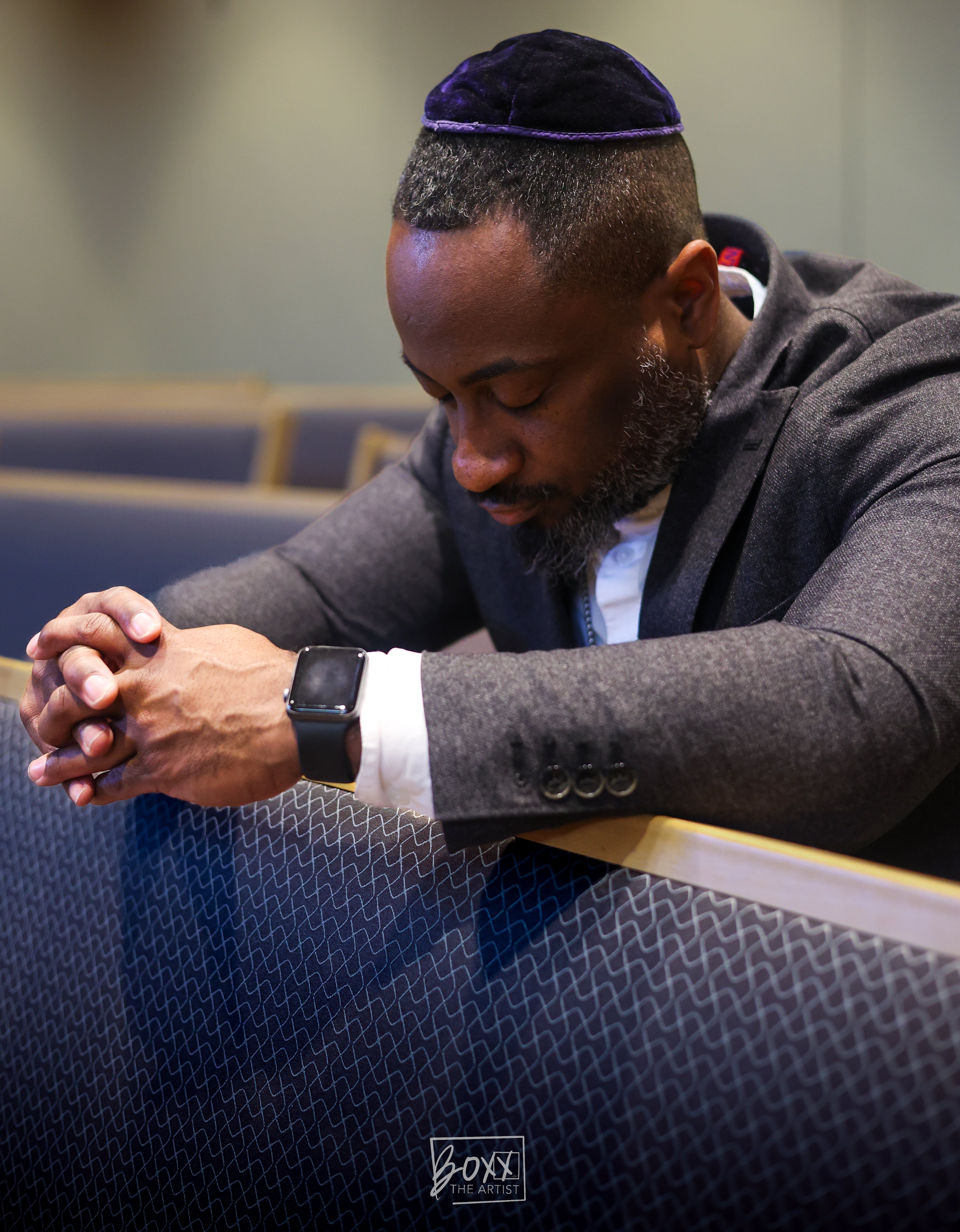 Man wearing a kippah sitting in a synagogue pew.