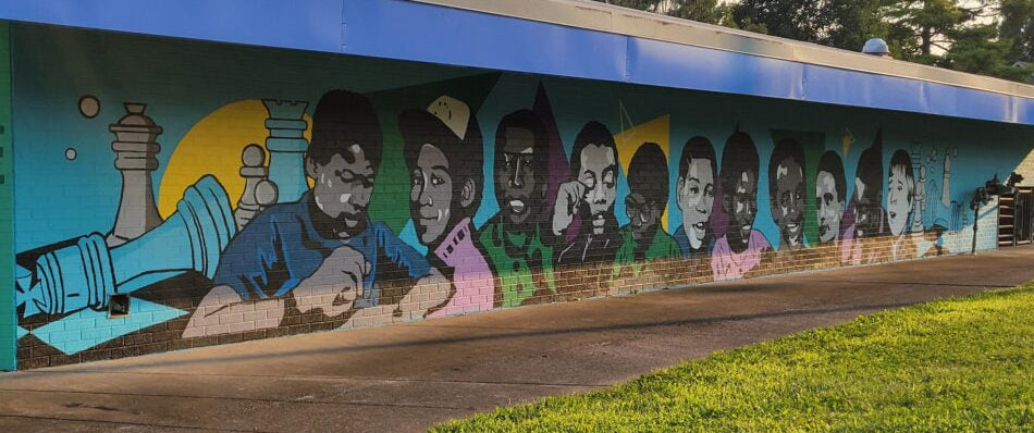 Mural of people on a wall with a blue border, grass, and trees in the background.